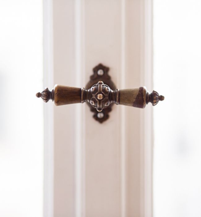 Detailaufnahme eines historischen Fenstergriffs mit kunstvollen Verzierungen aus Metall und Holz an einem weißen Altbaufenster.