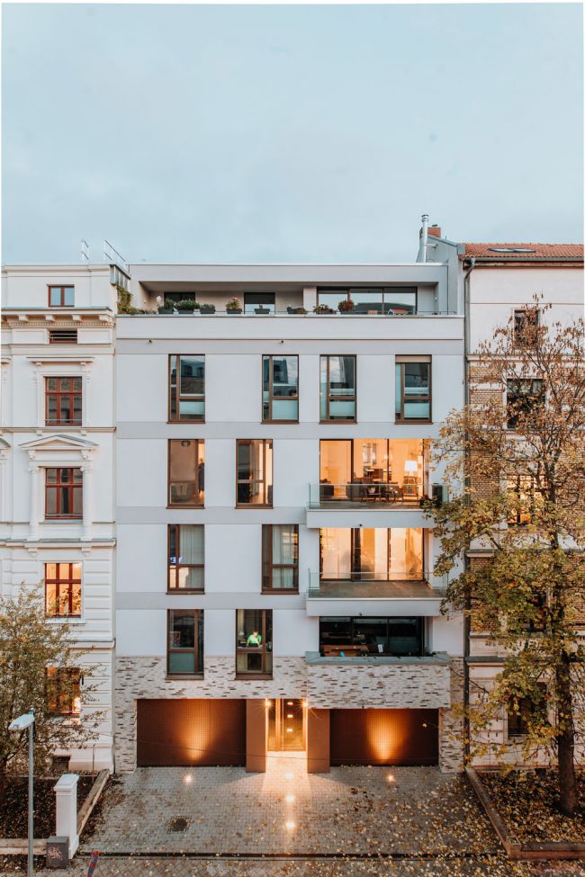 Modernes Stadthaus bei Dämmerung mit beleuchteten Fenstern und begrünten Balkonen.