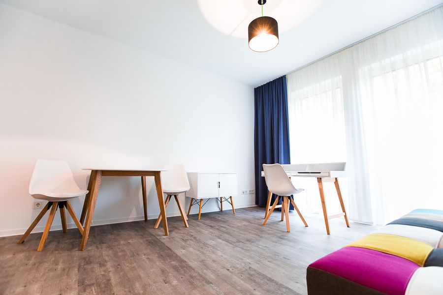 Modernes Arbeitszimmer mit minimalistischem Schreibtisch, Stühlen und farbenfrohem Sofa.