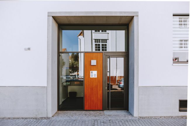 Modernes Eingangsdesign mit großer Glasfront und hölzerner Tür in urbaner Umgebung.