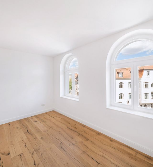 Helles Zimmer mit Parkettboden und großen, geschwungenen Fenstern mit Stadtblick.