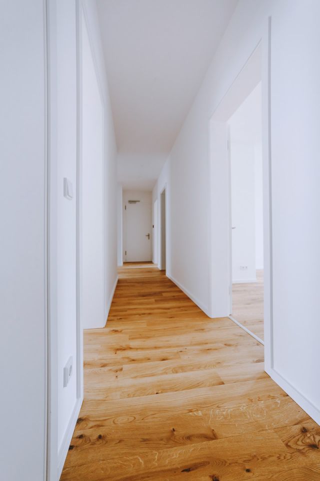 Langer, heller Flur mit Holzboden und weißen Türen in einem modernen Apartment.