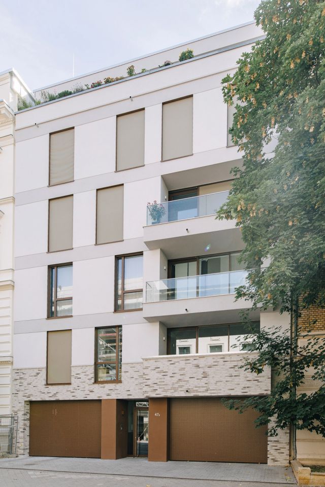 Modernes Gebäude mit Balkonen und begrüntem Dach in einem städtischen Viertel.