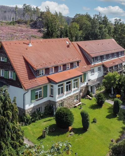 Landhaus mit rotem Dach und weißer Fassade, umgeben von Gärten und Wald.