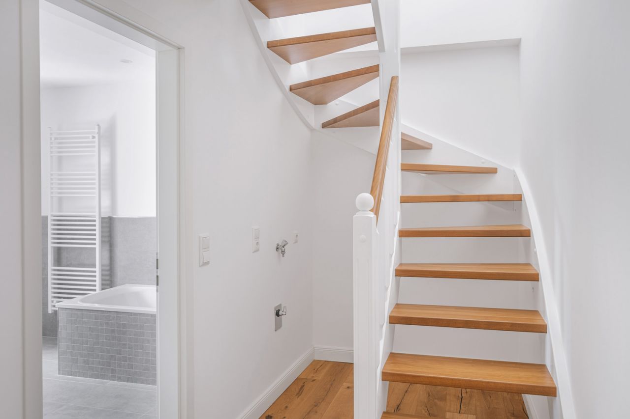 Moderne Holztreppe mit weißem Geländer neben einem stilvollen Badezimmer mit grauen Fliesen.