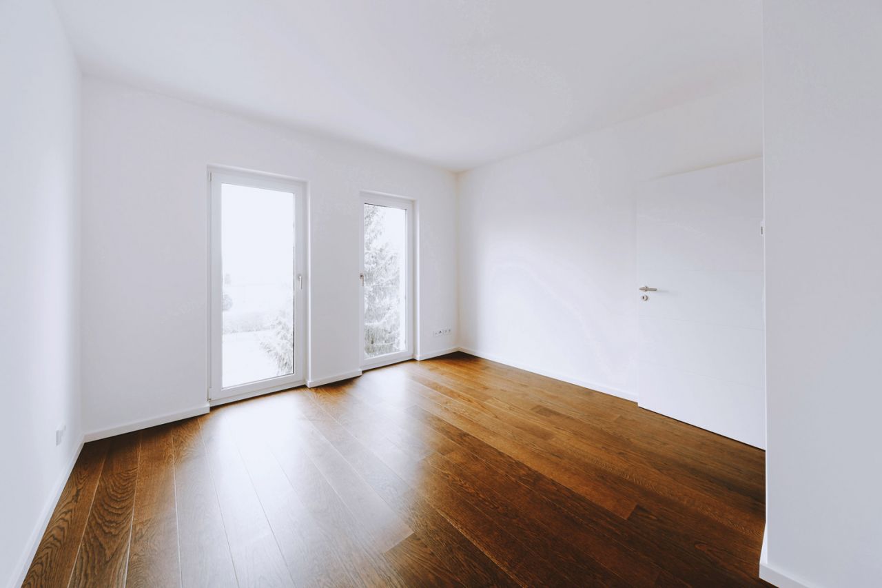 Helles, leeres Zimmer mit dunklem Holzboden und zwei Türen zur Terrasse.