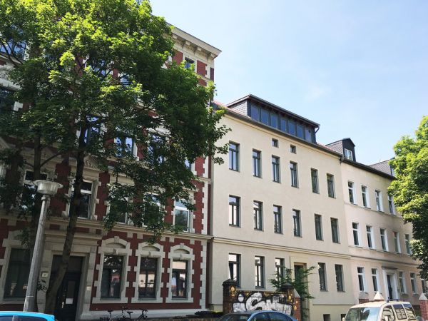 Sanierte Altbauten mit moderner Dachgeschosswohnung, große Fenster, begrünte Umgebung und urbane Wohnlage.