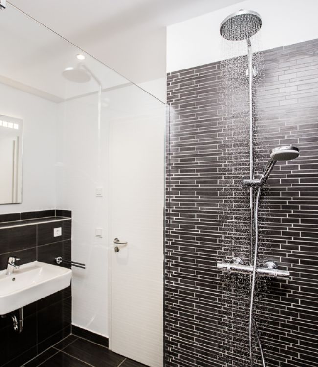 Modernes Badezimmer mit Regendusche und dunklen Fliesen. Stilvolles und schlichtes Design.