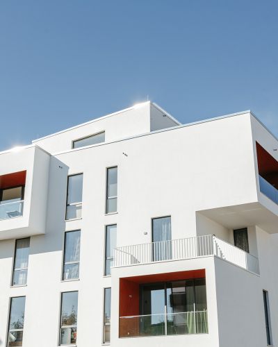 Modernes Wohngebäude mit weißen Fassaden und roten Akzenten unter klarem Himmel.
