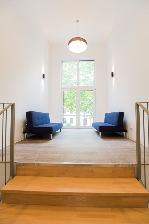 Heller Empfangsraum mit großen Fenstern, hohen Decken und zwei blauen Sesseln.