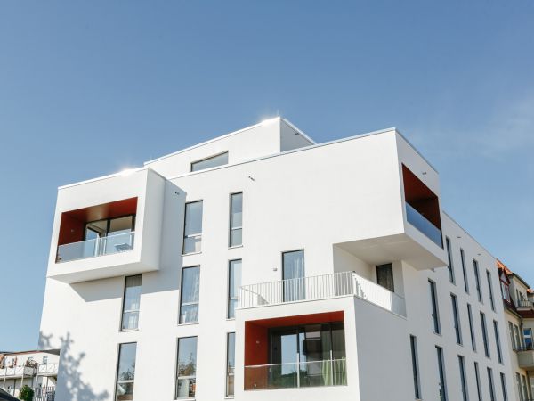 Modernes Wohngebäude mit weißen Fassaden und roten Akzenten unter klarem Himmel.