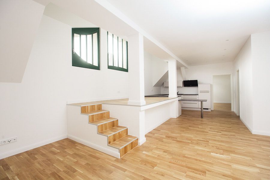 Modernes Loft mit offener Küche, stilvollen Holzböden und erhöhtem Wohnbereich mit einzigartigen Fenstern für viel Tageslicht.