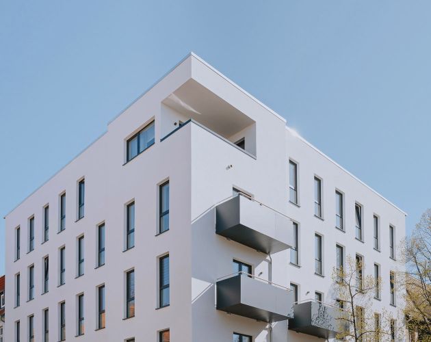Modernes Mehrfamilienhaus mit klarer Architektur, großen Fenstern und Balkonen.