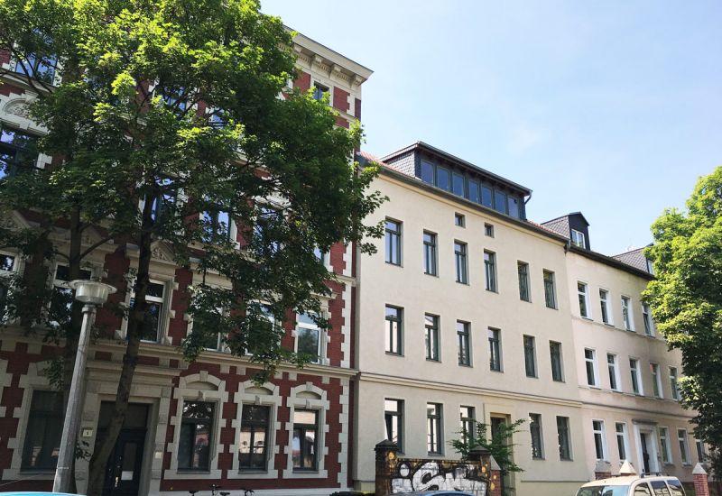 Sanierte Altbauten mit moderner Dachgeschosswohnung, große Fenster, begrünte Umgebung und urbane Wohnlage.
