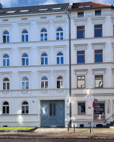 Historisches Stadthaus mit renovierter Fassade und blauer Eingangstür an einer Straßenecke.