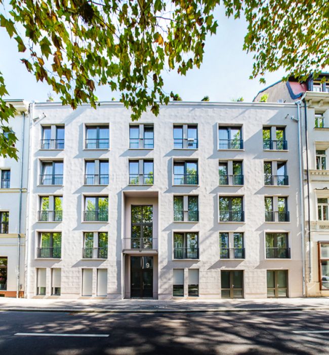 Modernes Stadthaus mit markanter Fassade neben traditionellen Gebäuden, umgeben von Bäumen.