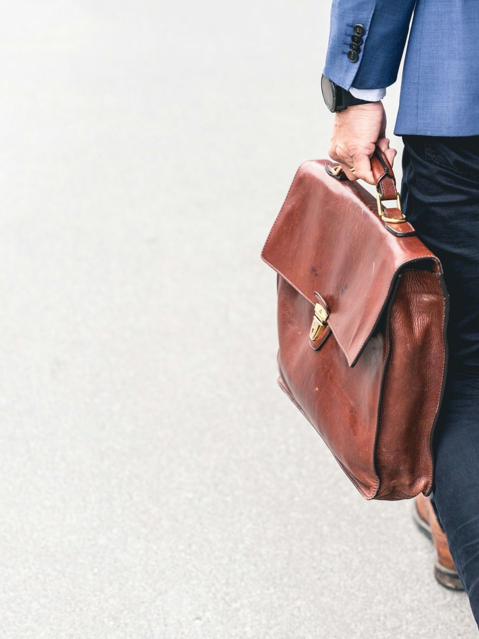 Geschäftsmann im Blazer trägt eine elegante Ledertasche auf einem Gehweg.