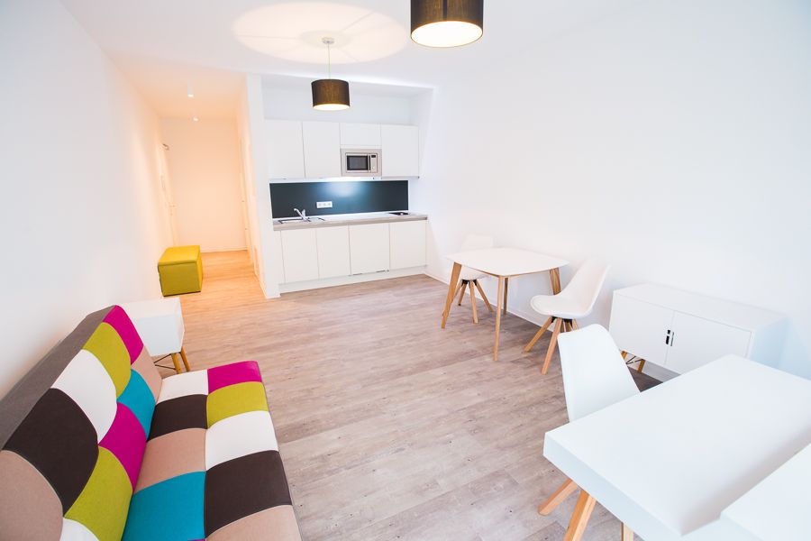 Modernes, helles Wohnzimmer mit buntem Sofa und integrierter Küche.