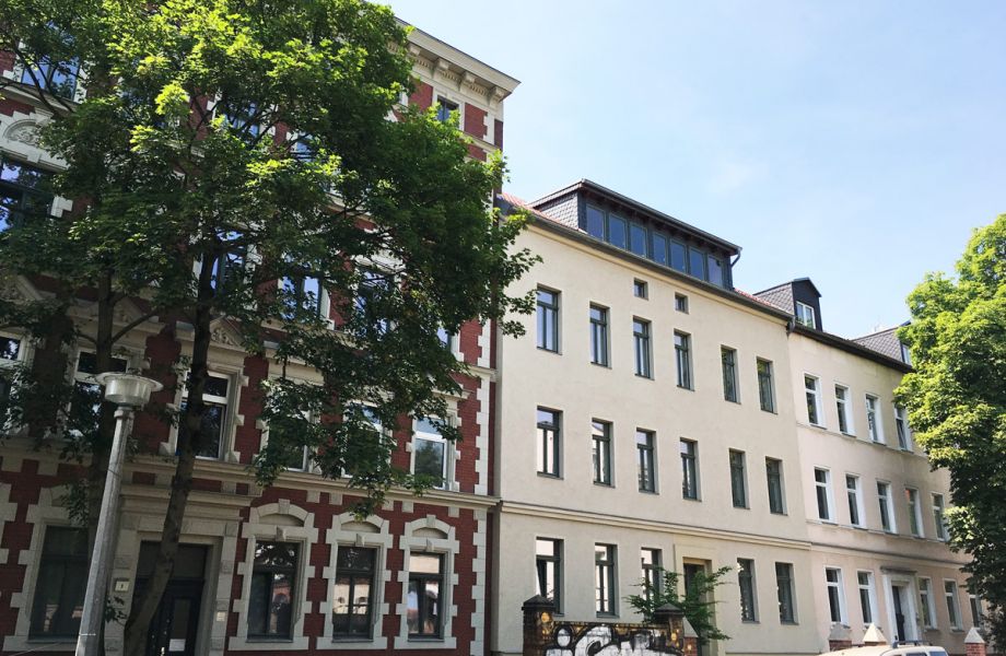 Sanierte Altbauten mit moderner Dachgeschosswohnung, große Fenster, begrünte Umgebung und urbane Wohnlage.