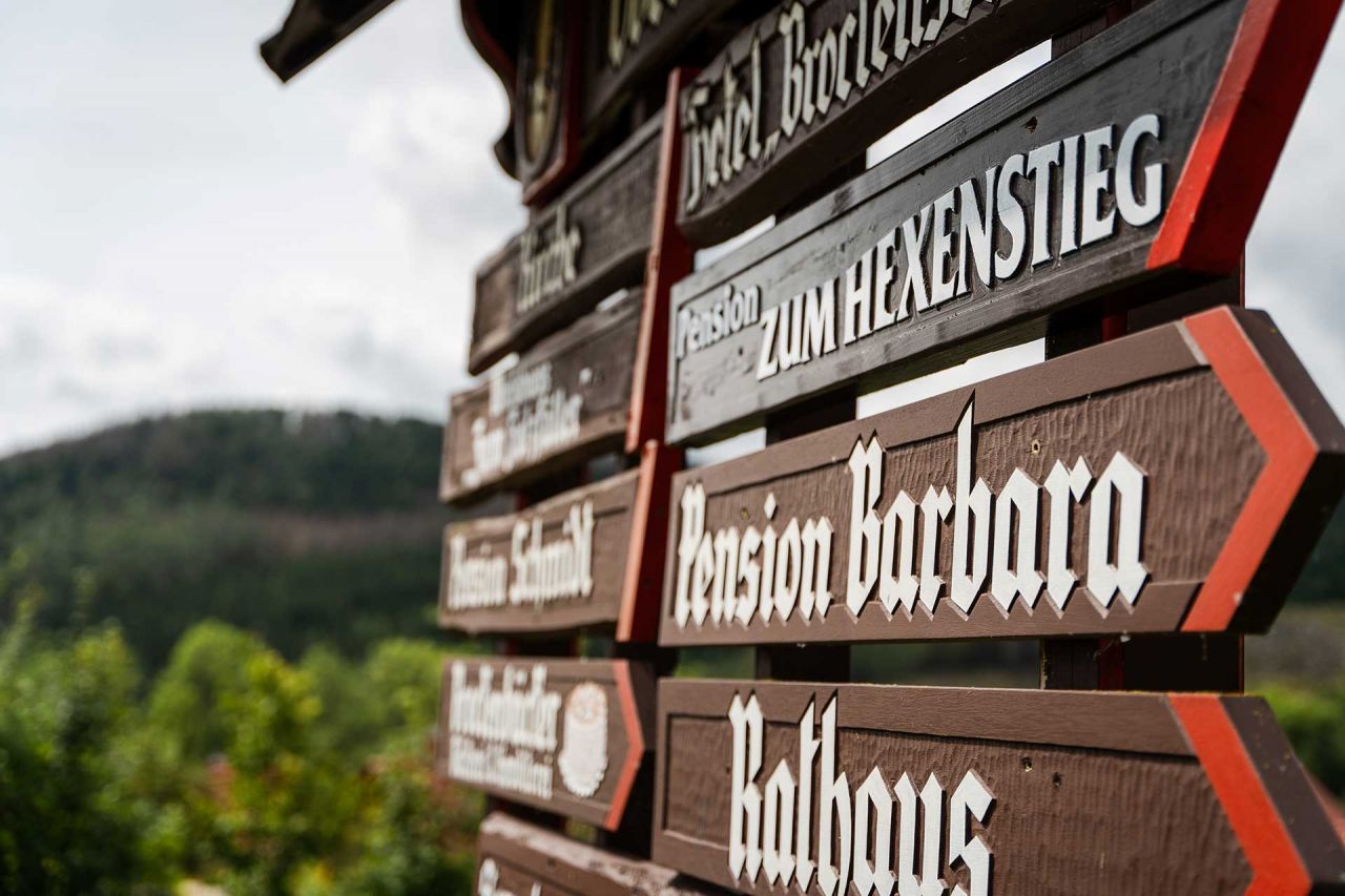 Holzwegweiser im Harz mit Schildern zu Pensionen und Sehenswürdigkeiten, darunter Pension Zum Hexenstieg und Rathaus.