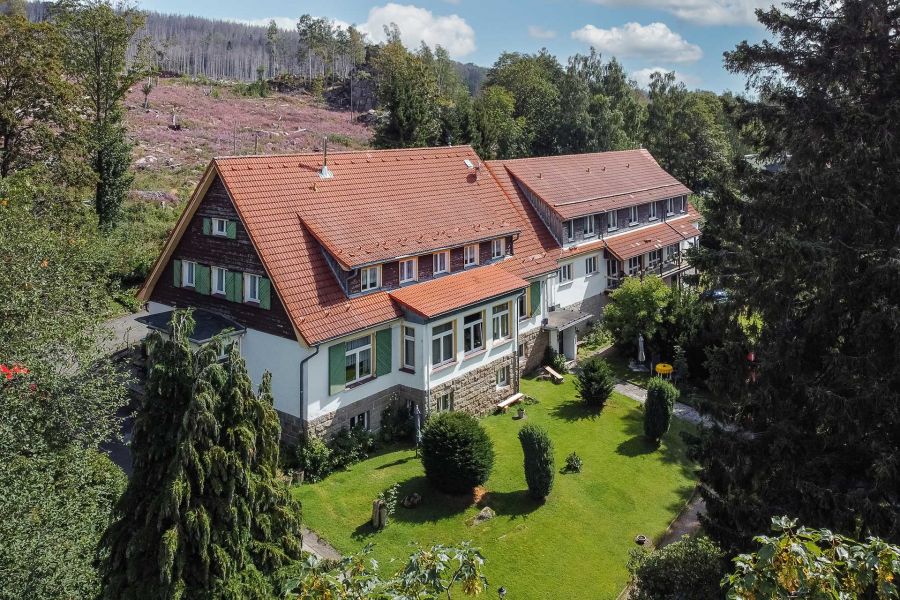 Landhaus mit rotem Dach und weißer Fassade, umgeben von Gärten und Wald.