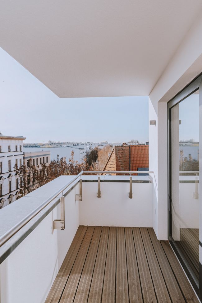 Moderner Balkon mit Holzboden und Geländer, mit Blick über die Stadt.