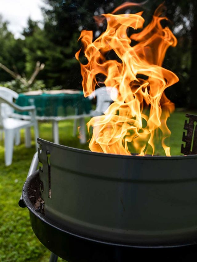 Grill mit loderndem Feuer in einem grünen Garten mit Sitzgelegenheiten – perfekte Atmosphäre für ein gemütliches Barbecue.