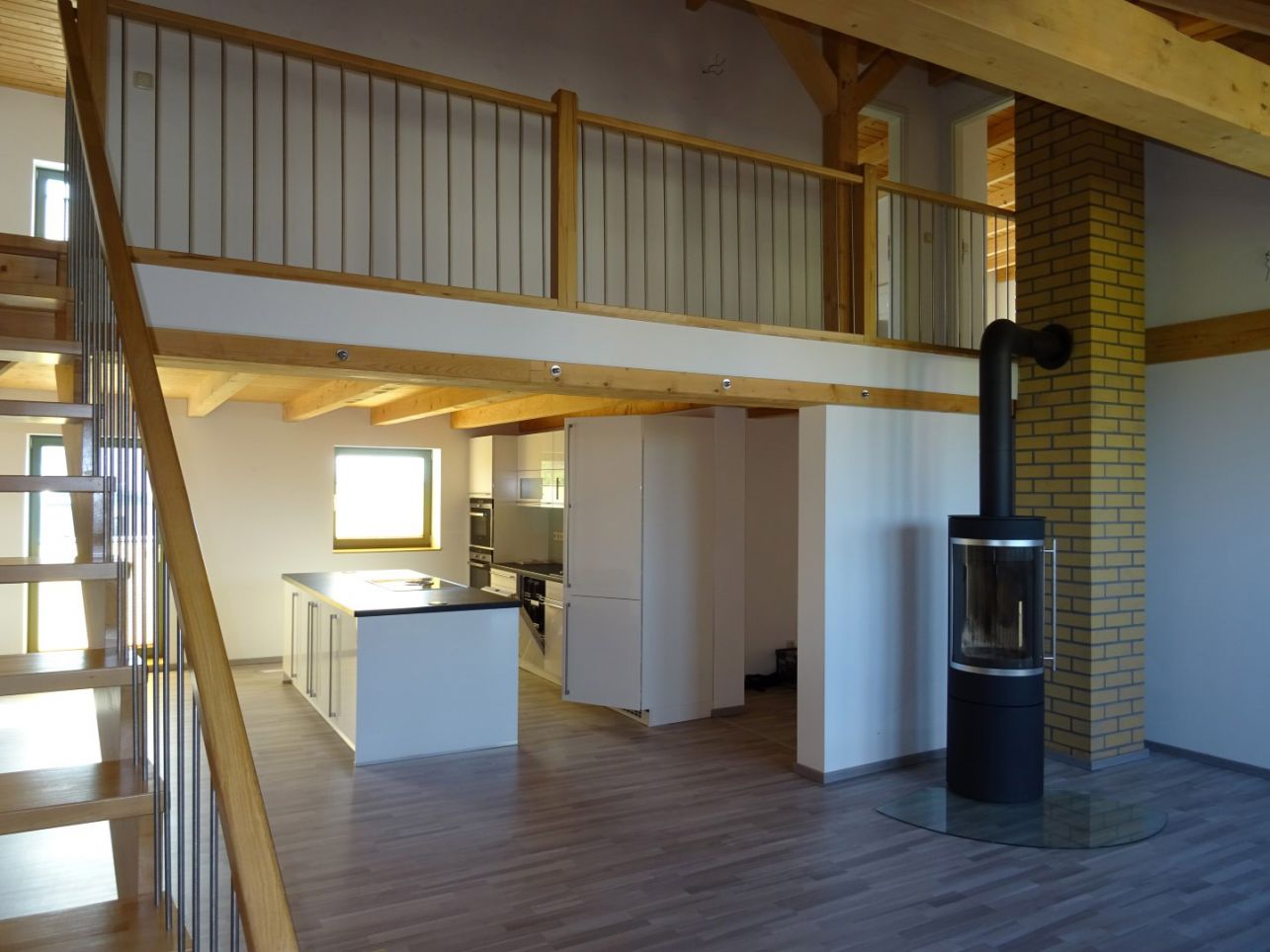 Moderne Loftwohnung mit offener Küche, Galerie und Kaminofen – stilvolles Wohnen mit Holz- und Metallelementen.