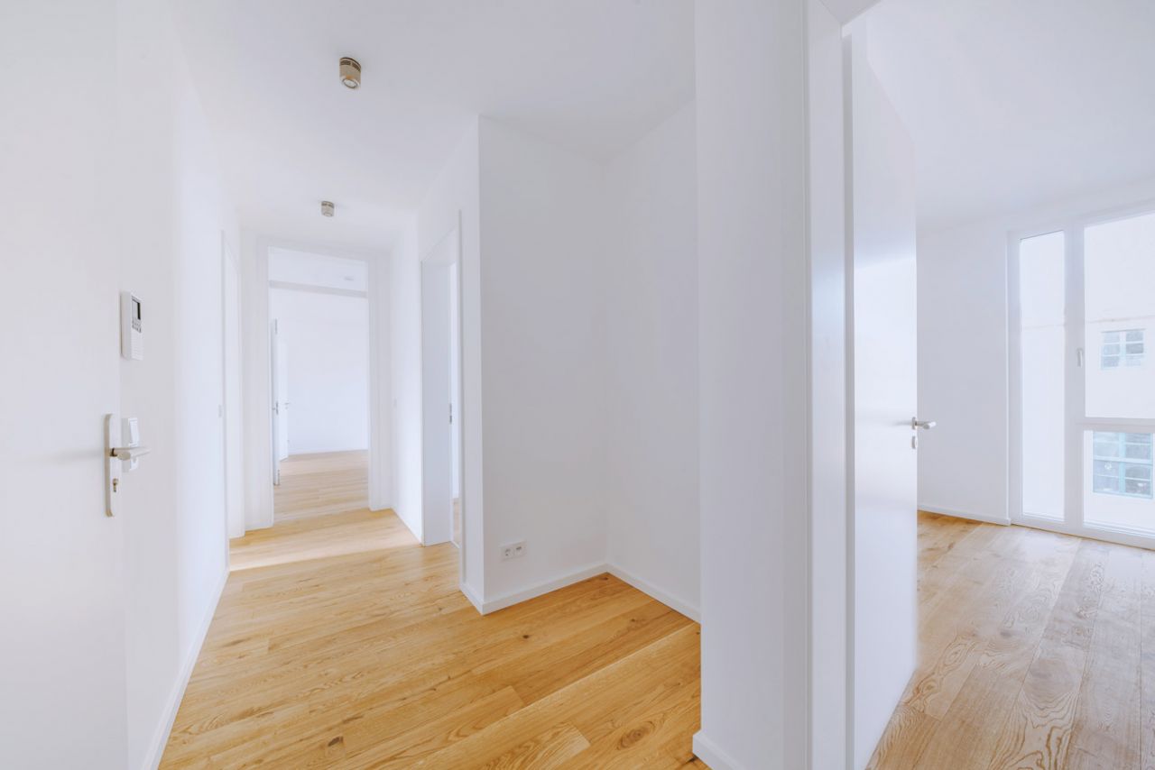 Helles, modernes Apartment mit Holzboden und weißen Wänden in einer Korridoransicht.