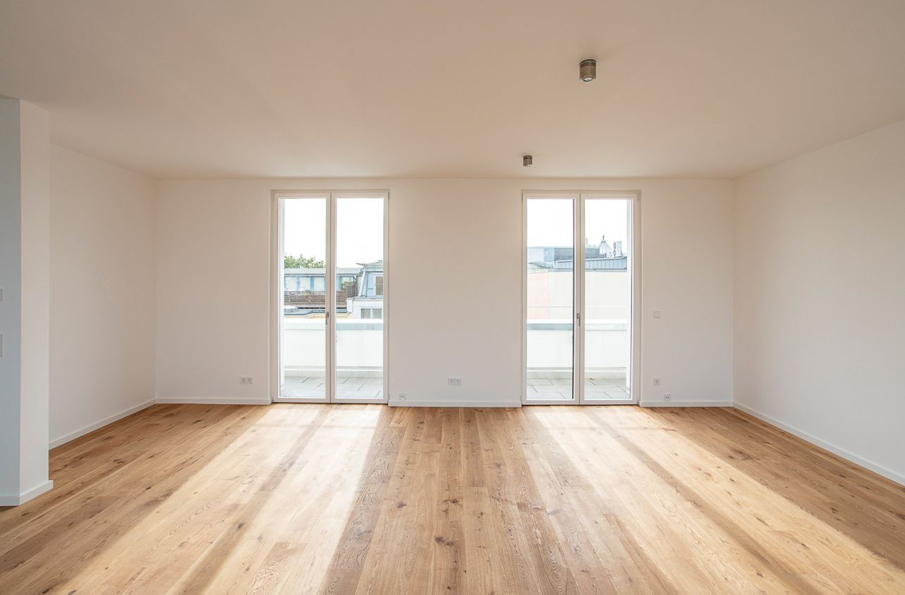 Geräumiges, helles Zimmer mit Holzfußboden und Zugang zu einem Balkon.