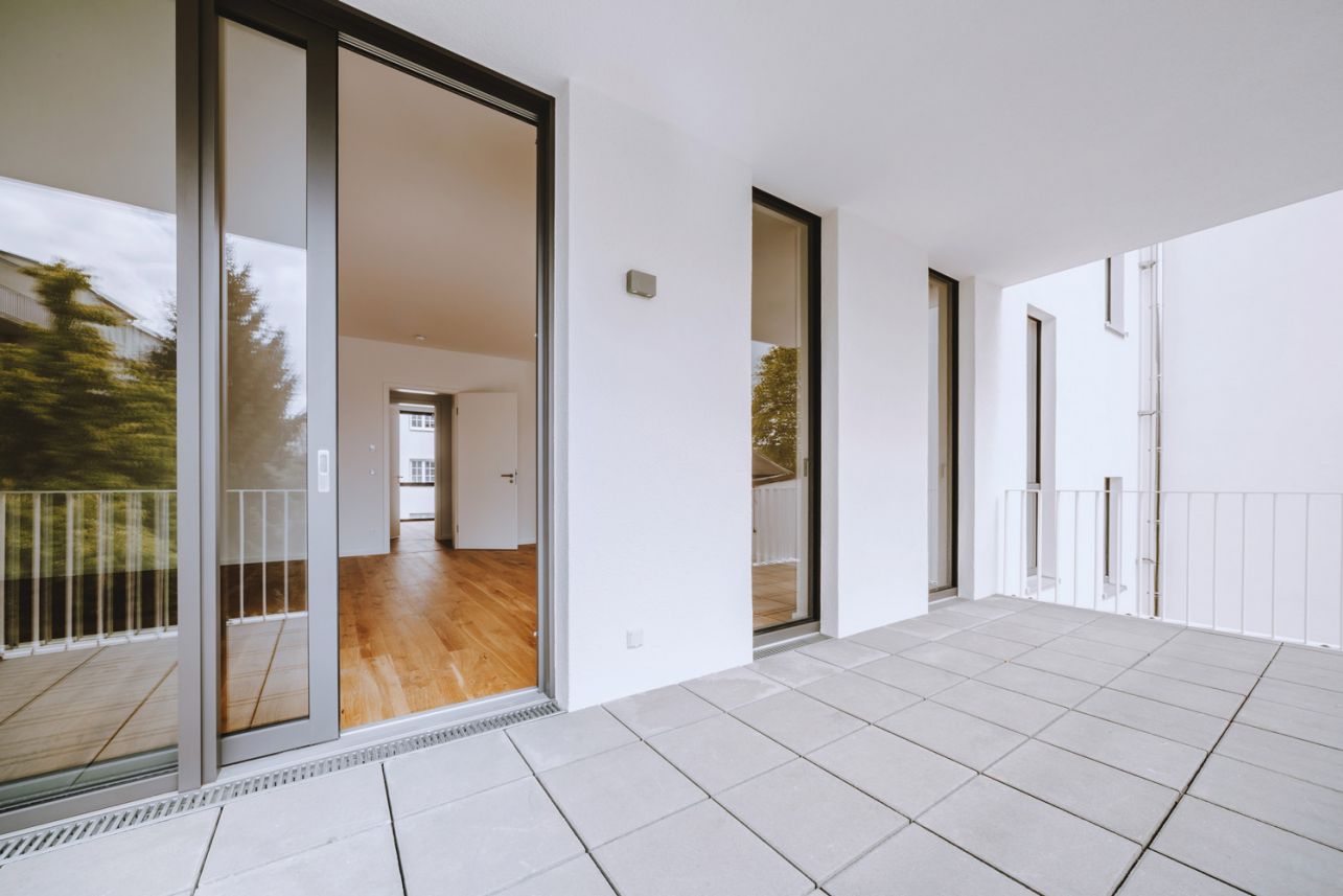 Geräumige Terrasse einer modernen Wohnung mit Holzboden und großen Glastüren.