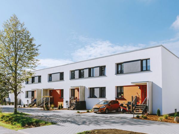 Moderne Reihenhäuser mit farbigen Eingangstüren und gepflastertem Vorplatz an einem sonnigen Tag.