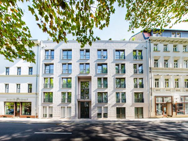 Modernes Stadthaus mit markanter Fassade neben traditionellen Gebäuden, umgeben von Bäumen.