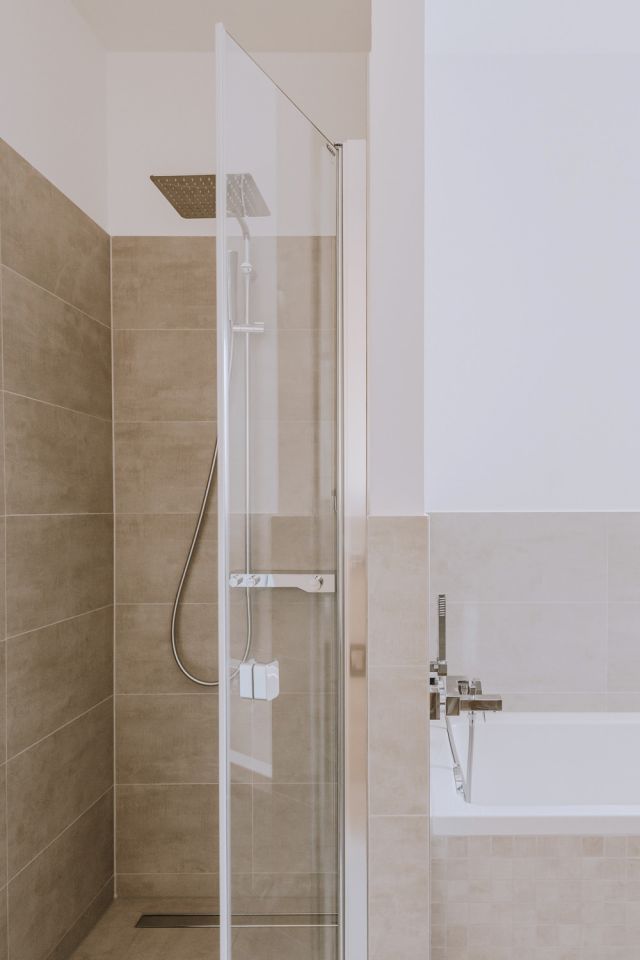 Modernes Badezimmer mit ebenerdiger Dusche, Glasabtrennung und Badewanne in stilvollem Beige-Fliesendesign.