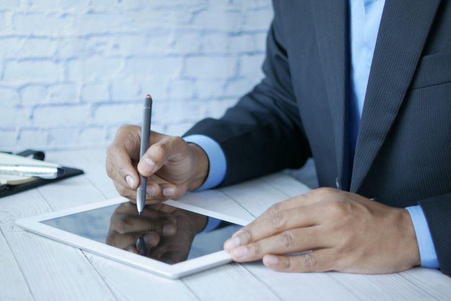Geschäftsmann arbeitet mit Tablet und Stylus an einem Holztisch.