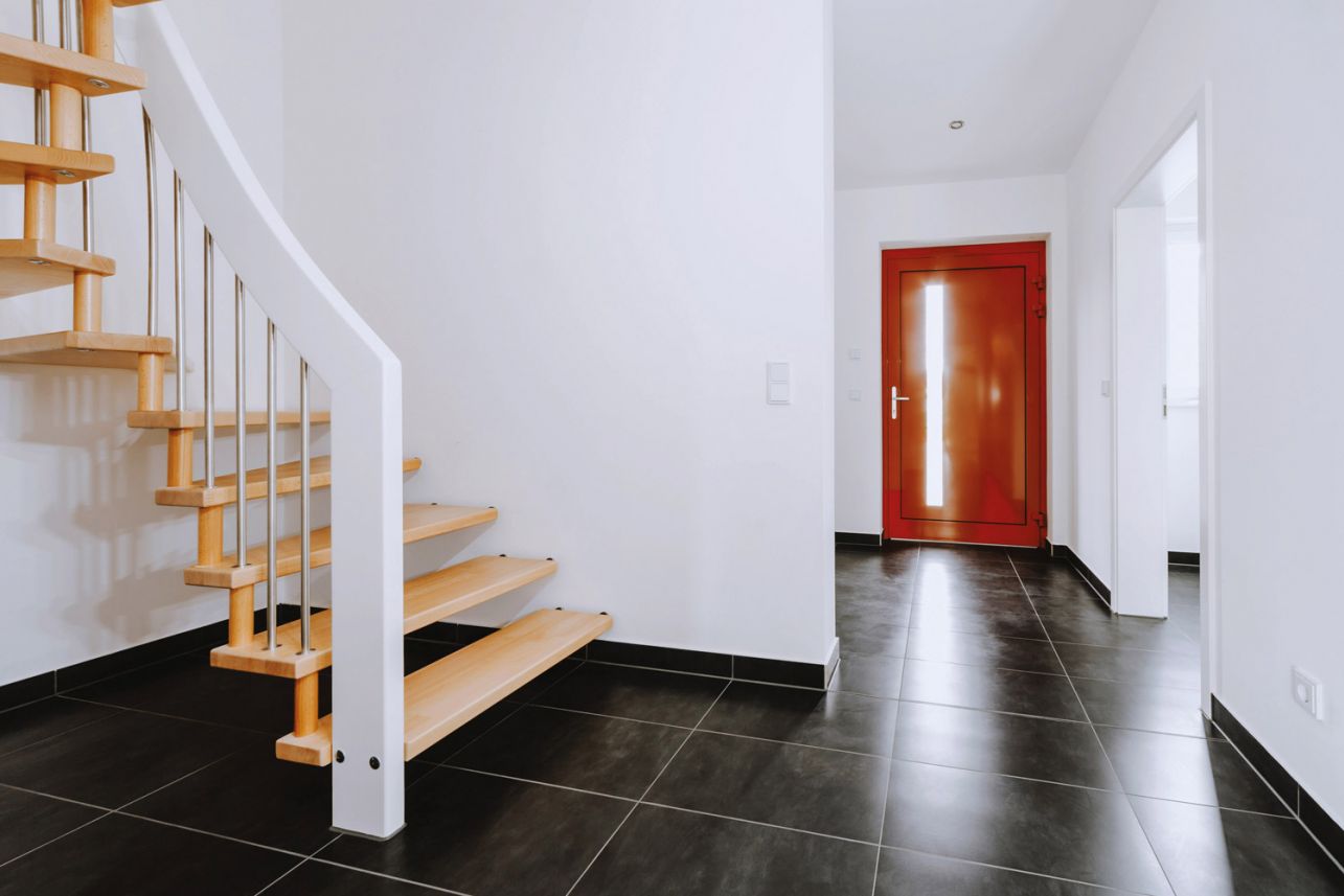 Moderner Eingangsbereich mit Holztreppe, schwarzen Fliesen und roter Haustür.
