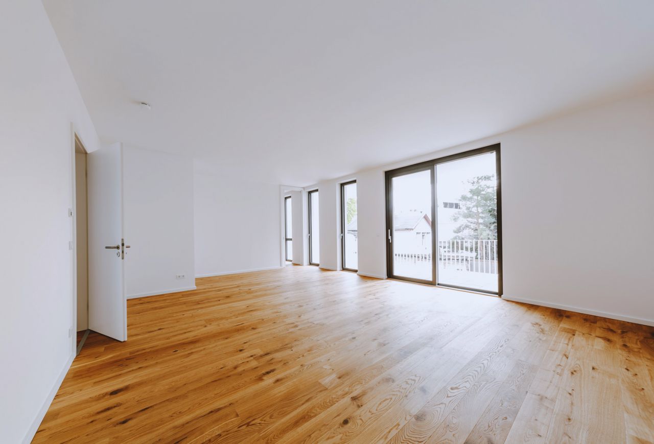 Helles, geräumiges Wohnzimmer mit Holzfußboden und großen Fenstern.