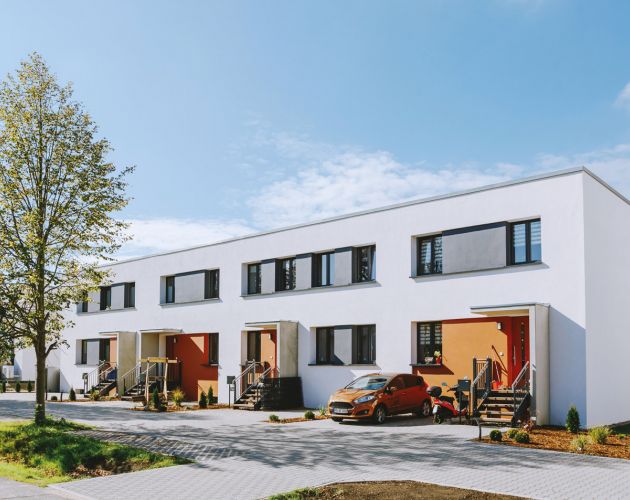 Moderne Reihenhäuser mit farbigen Eingangstüren und gepflastertem Vorplatz an einem sonnigen Tag.